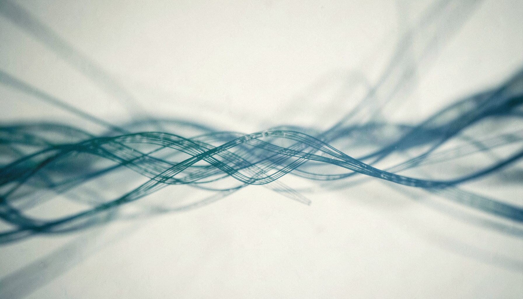 A cinematic wide frame with shallow depth of field showing abstract flowing data lines in muted teal and slate-blue against a dark background