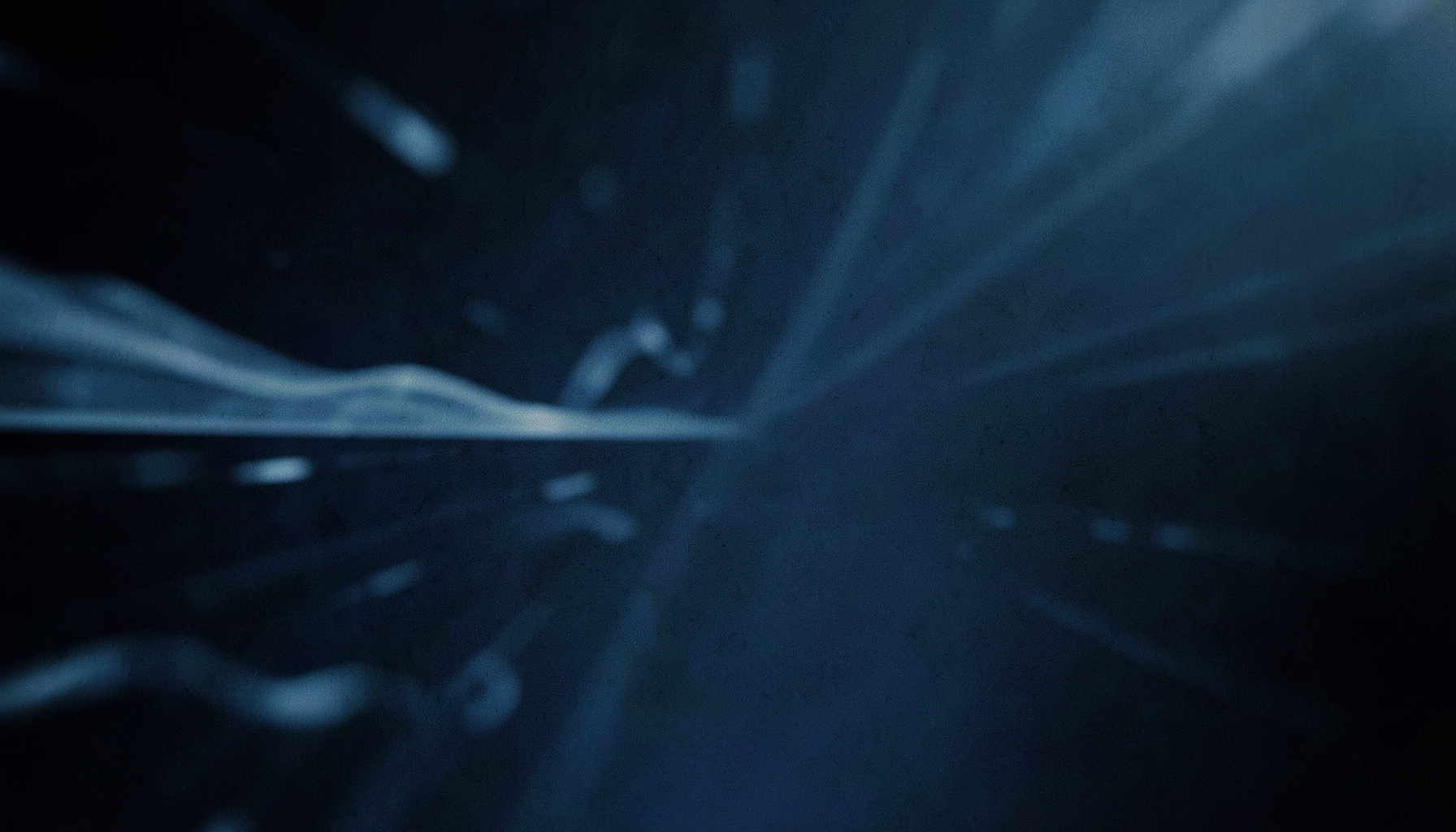 A cinematic wide frame with shallow depth of field showing soft blue-gray abstract data patterns and subtle light streaks across a dark gradient background